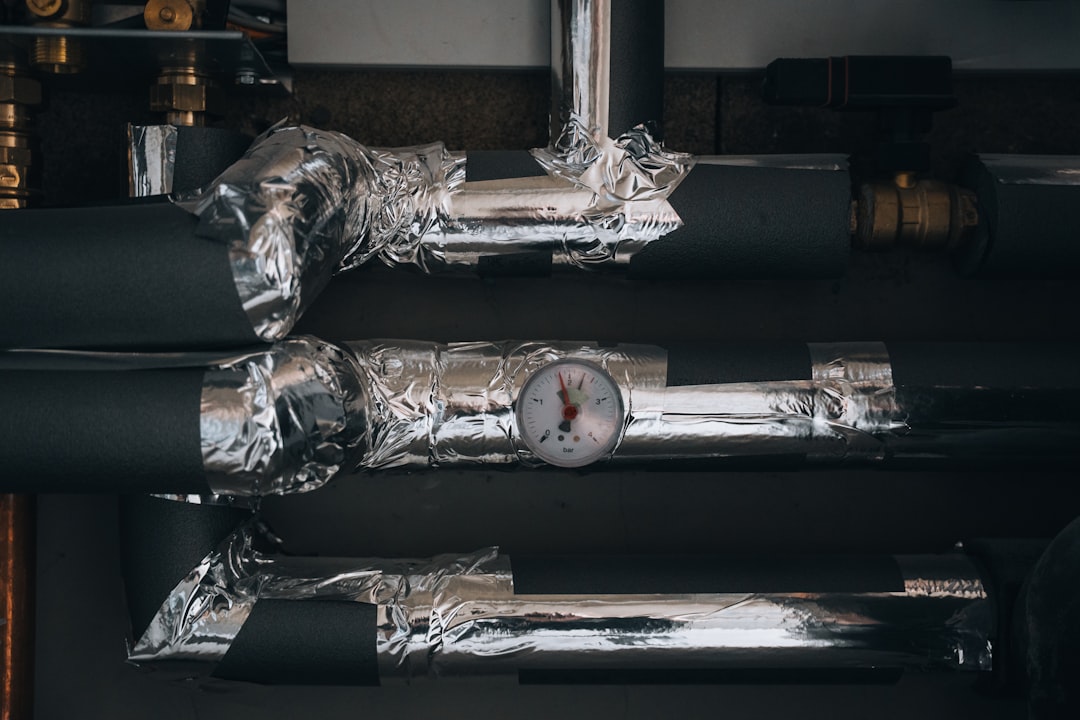 A network of insulated heating or plumbing pipes, wrapped in silver foil tape, features a central pressure gauge indicating system status. The image highlights industrial efficiency and technical precision in utility infrastructure.